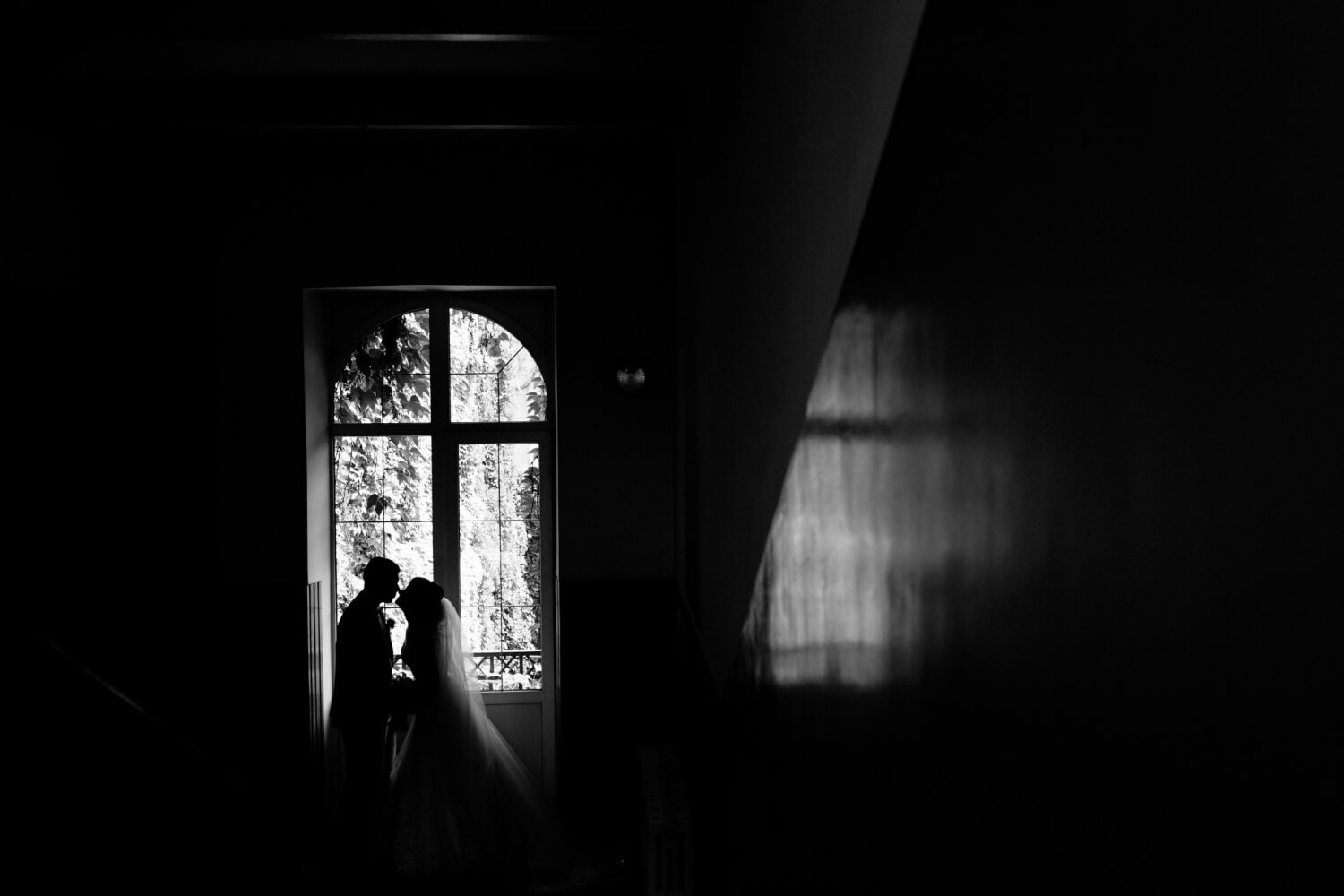 monochrome view silhouette wedding couple which is nearly kissing near window.jpg
